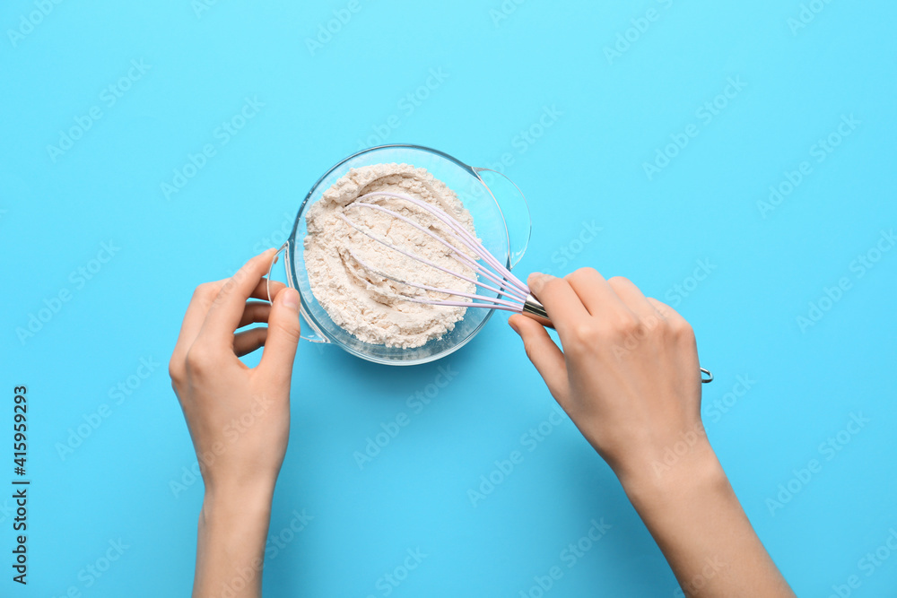 Female hands, whisk and bowl with flour on color background