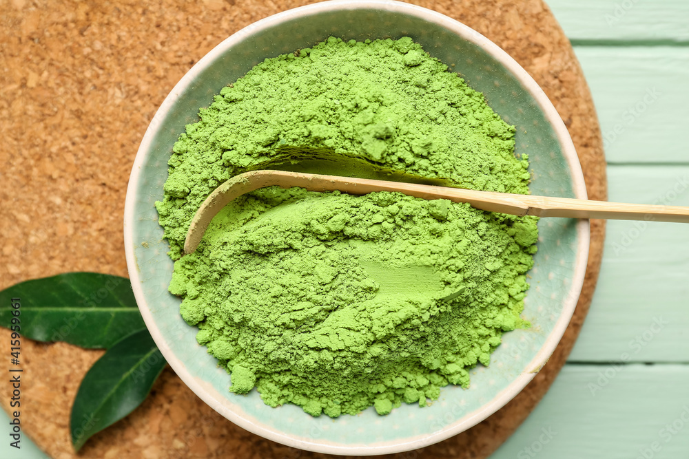 Bowl with powdered matcha tea and chashaku on color wooden background, closeup