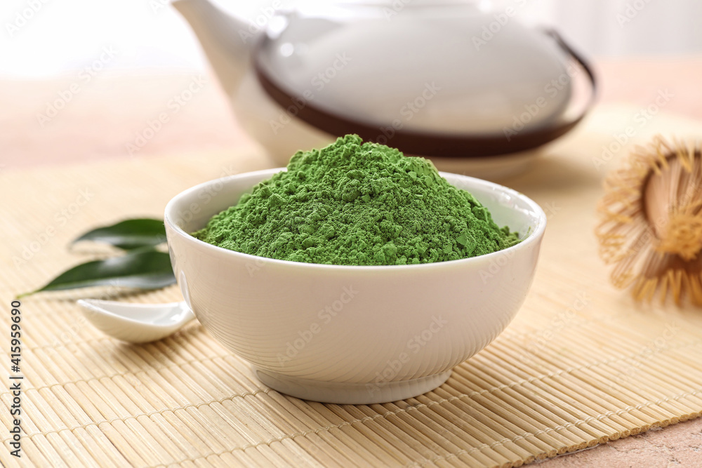 Bowl with powdered matcha tea and teapot on table, closeup