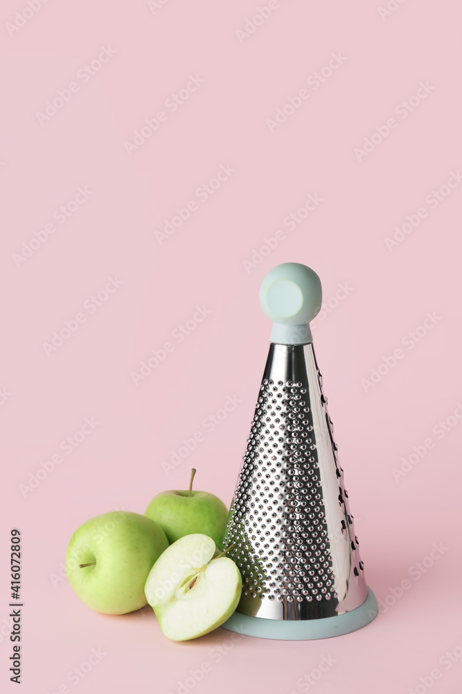 Metal grater and apples on color background