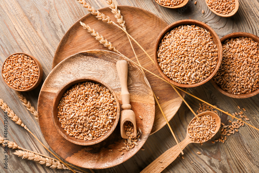 Bowls and spoons with wheat grains on wooden background