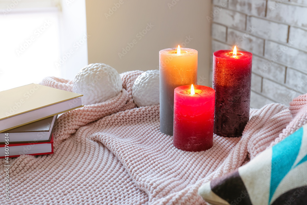 Burning candles on plaid in room