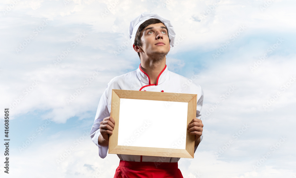 Young male chef holding blank white board