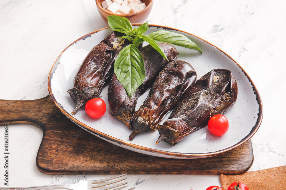 Plate of tasty baked eggplant with tomatoes on light background