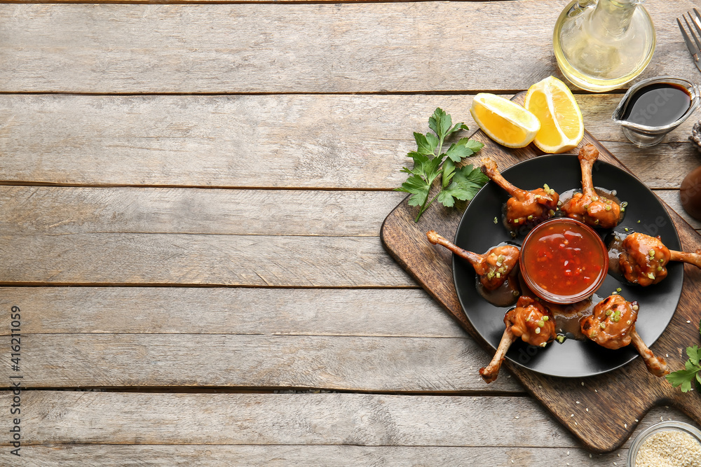 Plate with tasty chicken lollipops and sauce on wooden background