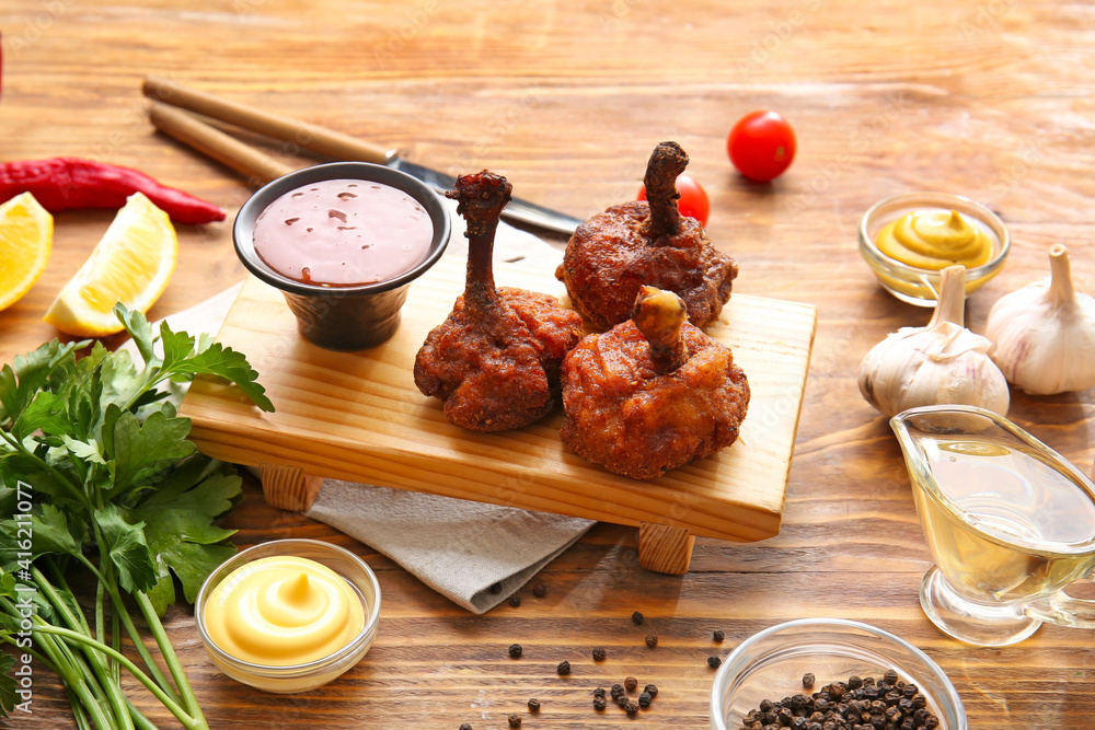 Board with tasty chicken lollipops and sauce on wooden background