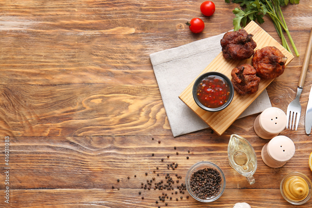 Board with tasty chicken lollipops and sauce on wooden background