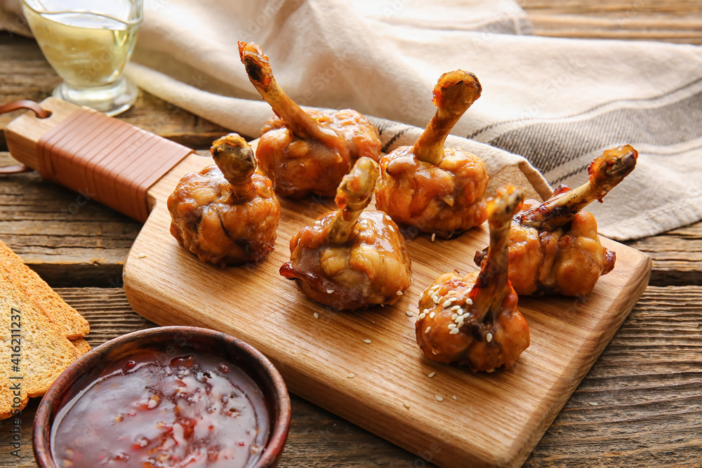 Board with tasty chicken lollipops on wooden background