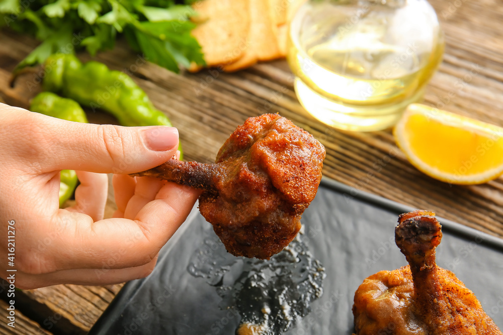 Woman eating tasty chicken lollipops on wooden background