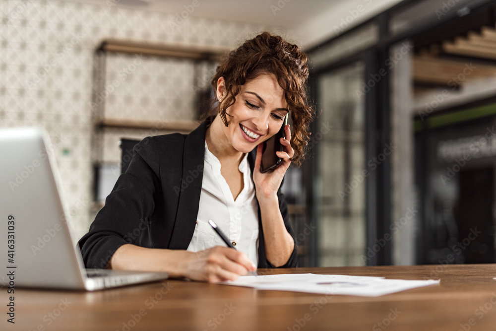 Woman writing some notes, while talking with someone over the phone.