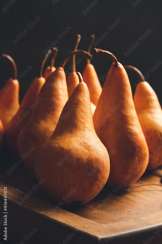 Board with fresh ripe pears on dark background