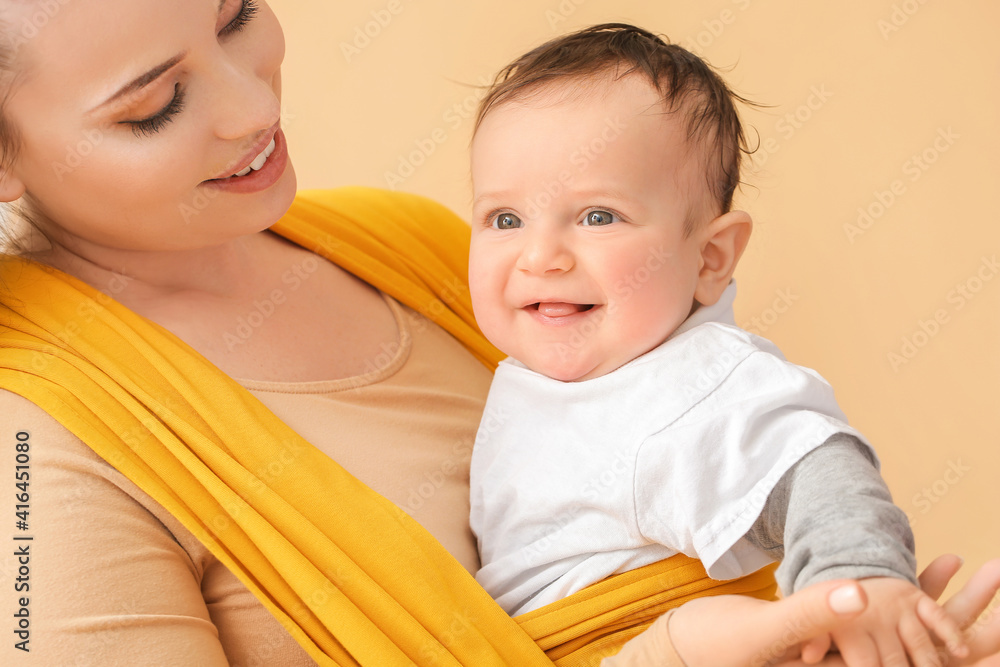 Young mother with little baby in sling on light background