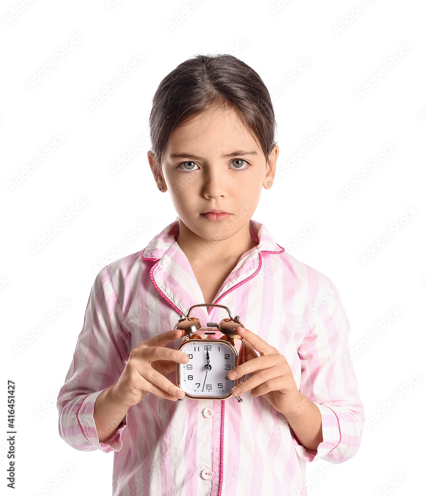 Sad little girl in pajamas and with alarm clock on white background