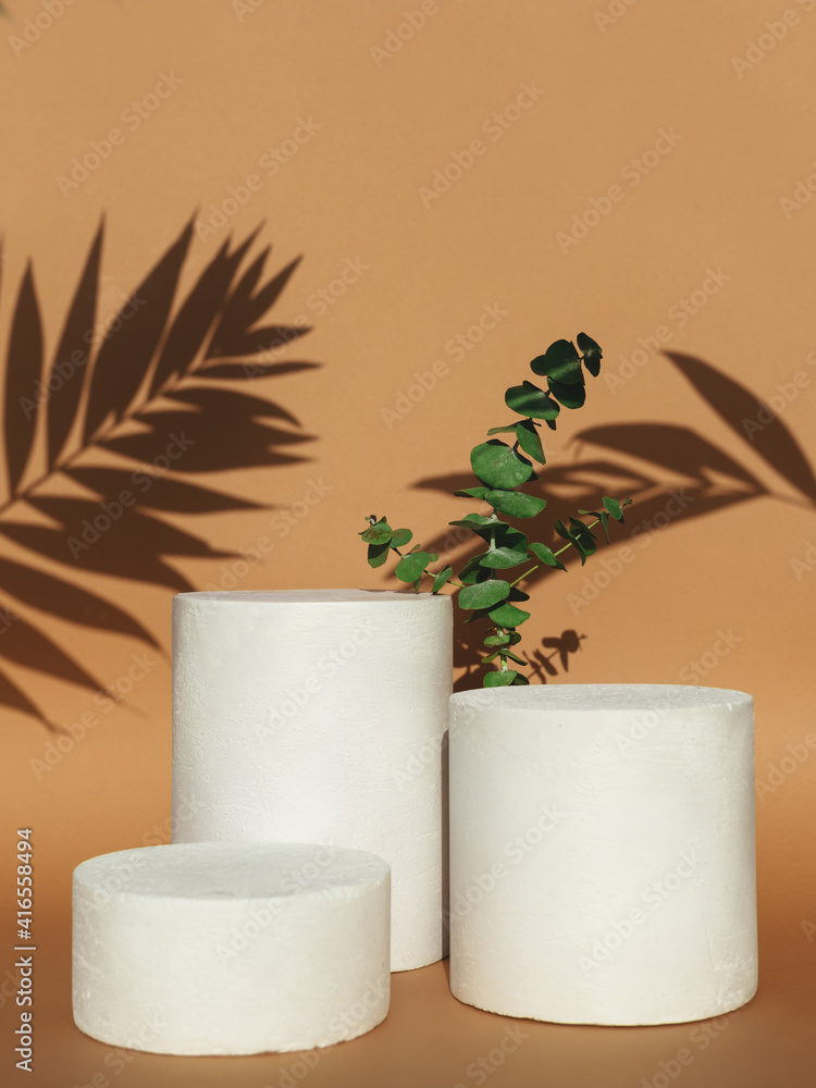 Empty background for cosmetic products. Podiums with green leaves and shadow on beige background.