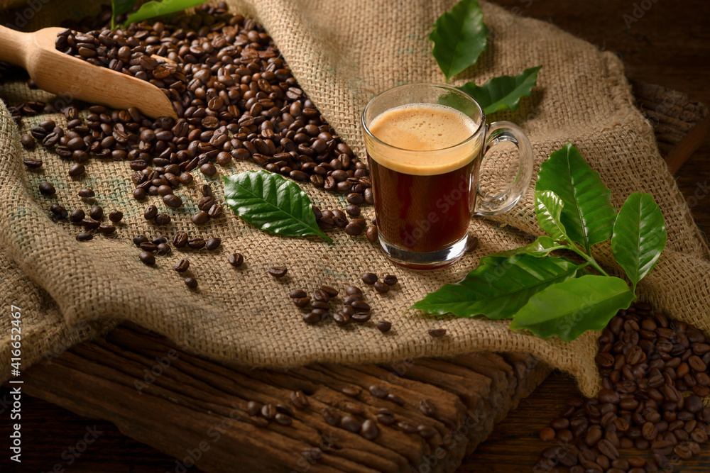 Cup glass of coffee with smoke and coffee beans on burlap sack on old wooden background