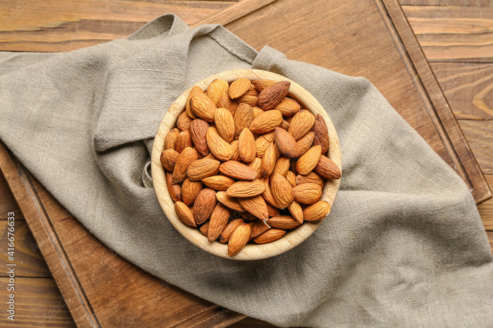 Bowl with tasty almonds on wooden background