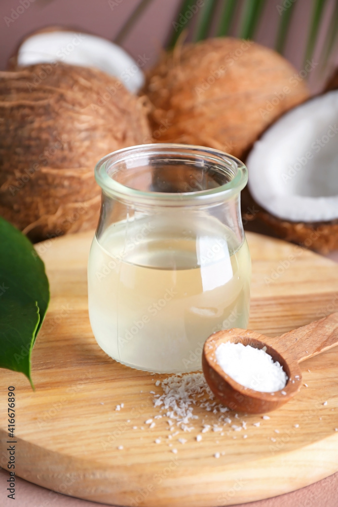 Jar of coconut oil and spoon with flakes on color background