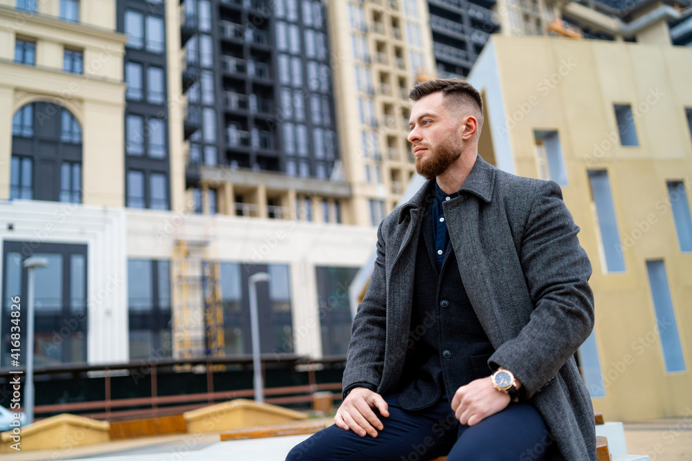 Man in formal clothes sitting on a street bench with hands on legs. Fashion and stylish handsome you