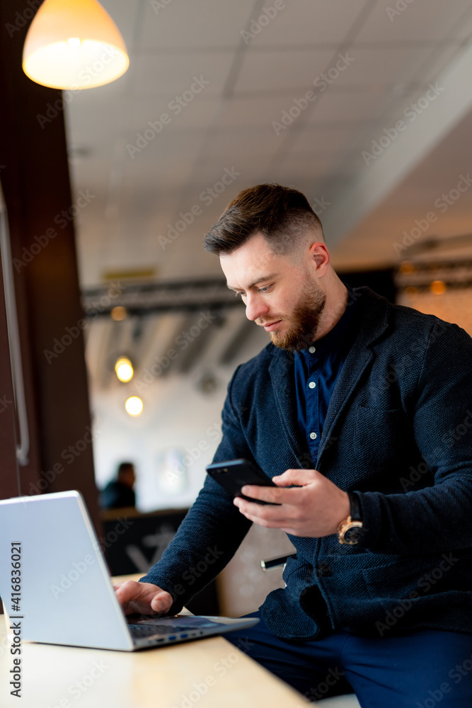 Businessman in formal clothes sits in cafe with laptop and phone in hands. Handsome and stylish youn