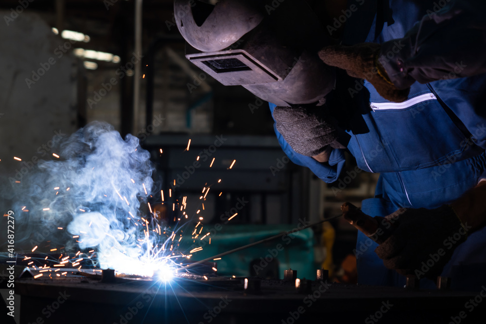 Skillful metal worker working with arc welding machine in factory while wearing safety equipment. Me