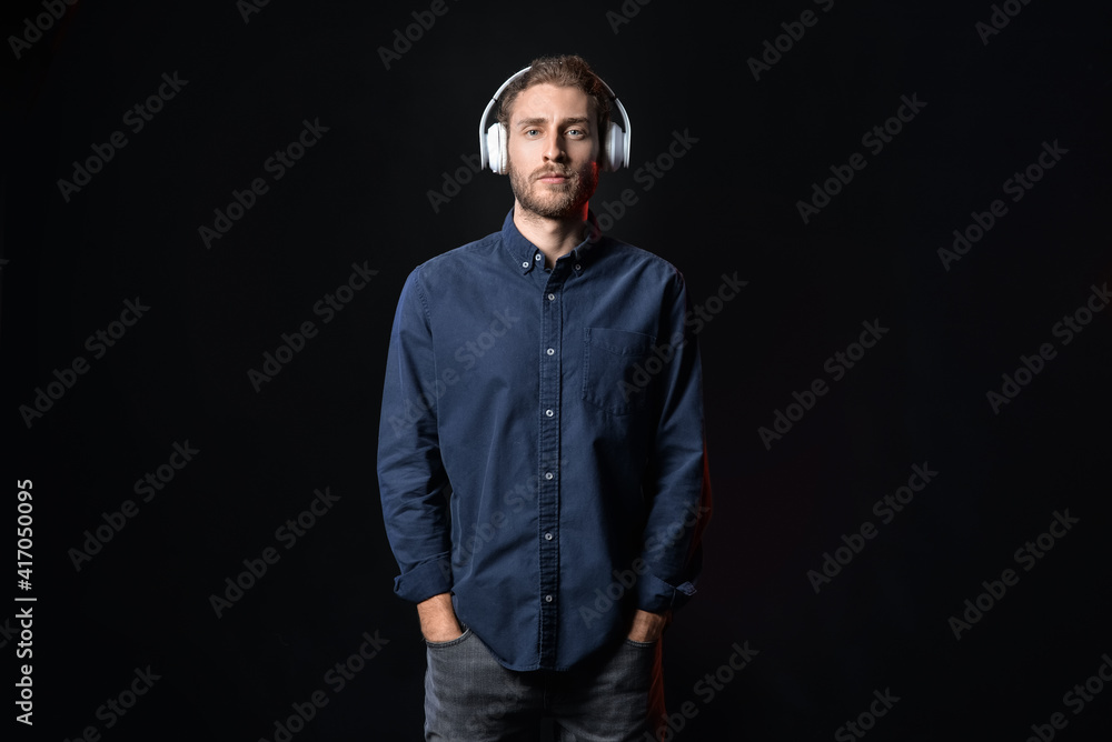 Handsome young man listening to music on dark background