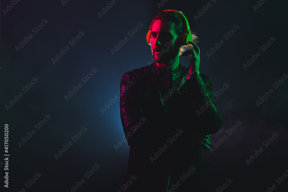 Handsome young man listening to music on dark background