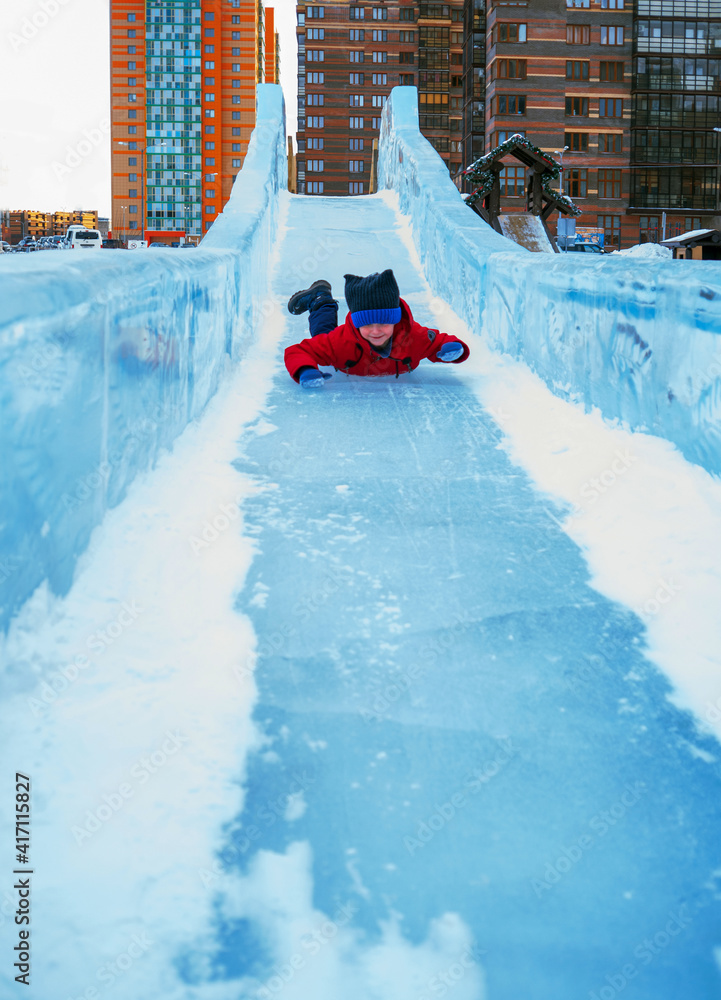 Caucasian boy is rolling down along ice slide. Winter outdoor activities.