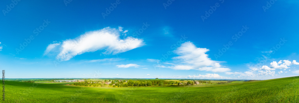 Panorama of a green field and sky. Sunny summer landscape of a European village