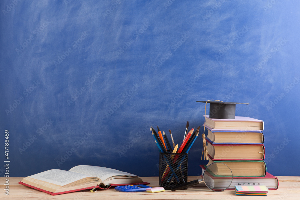 Education and sciences concept - books on the teacher desk in the auditorium, chalkboard on the back