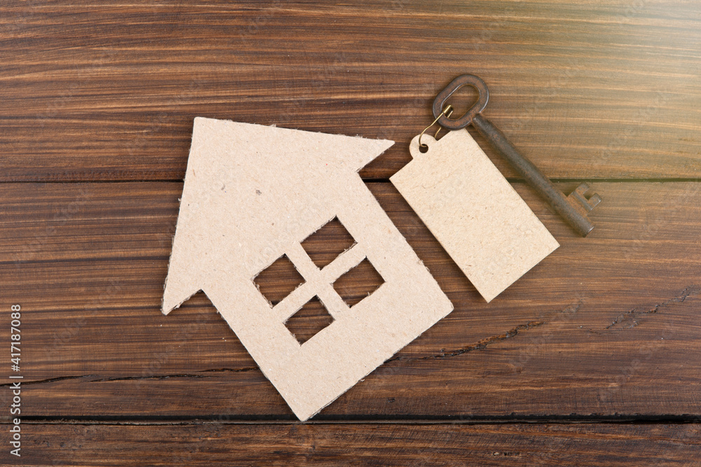 Real estate concept -Buying,selling or rent a house. Old key with tag and cardboard house on wooden 