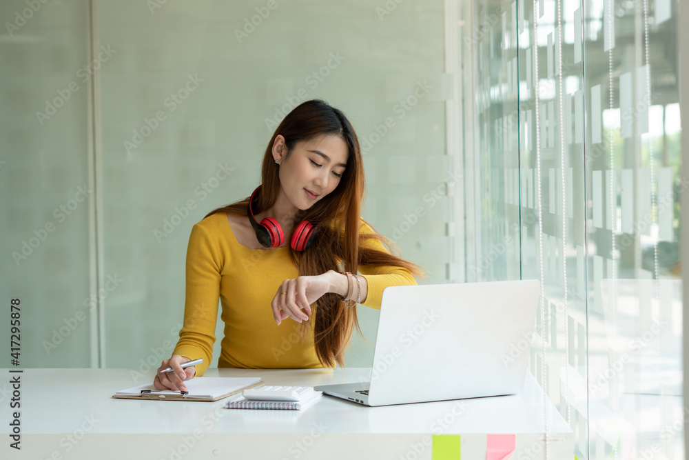 The portrait of an Asian business woman looks at her watch at work. A woman starts checking time on 