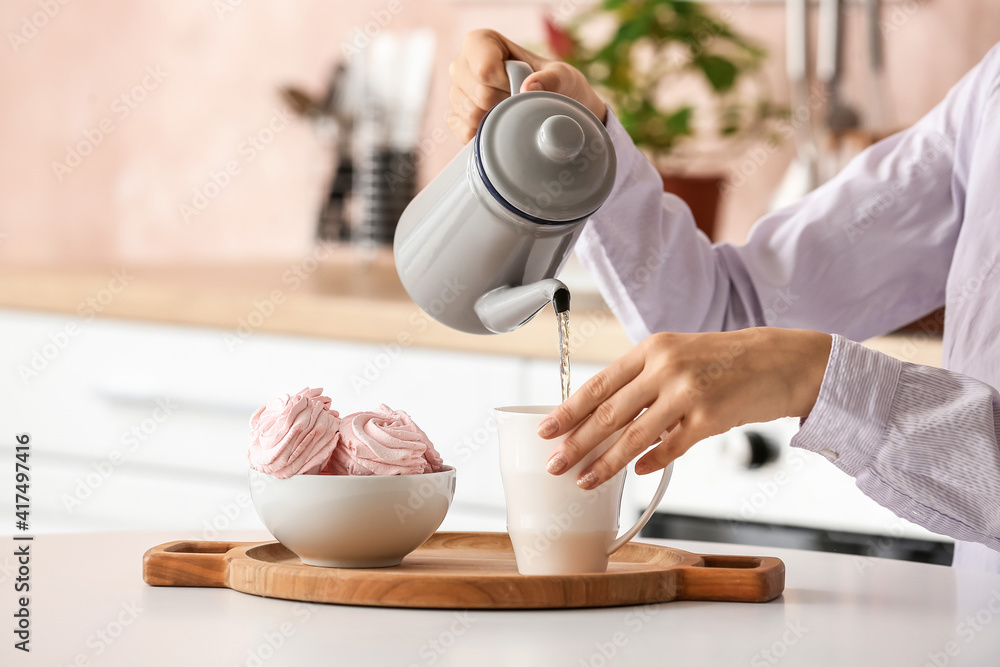 女人在厨房把茶壶里的茶倒进杯子里