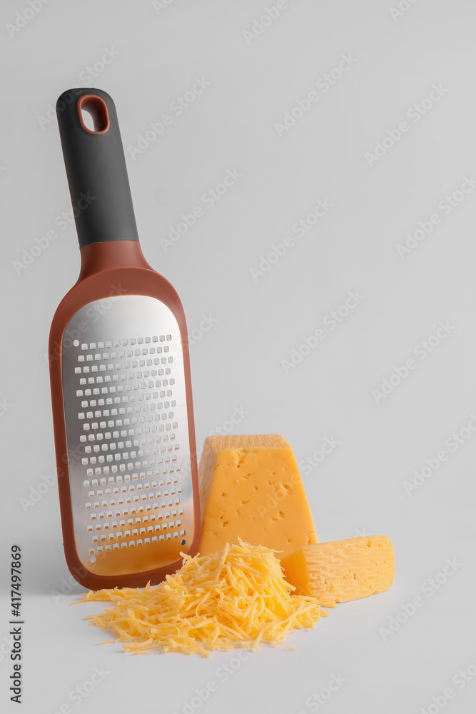 Metal grater and cheese on light background