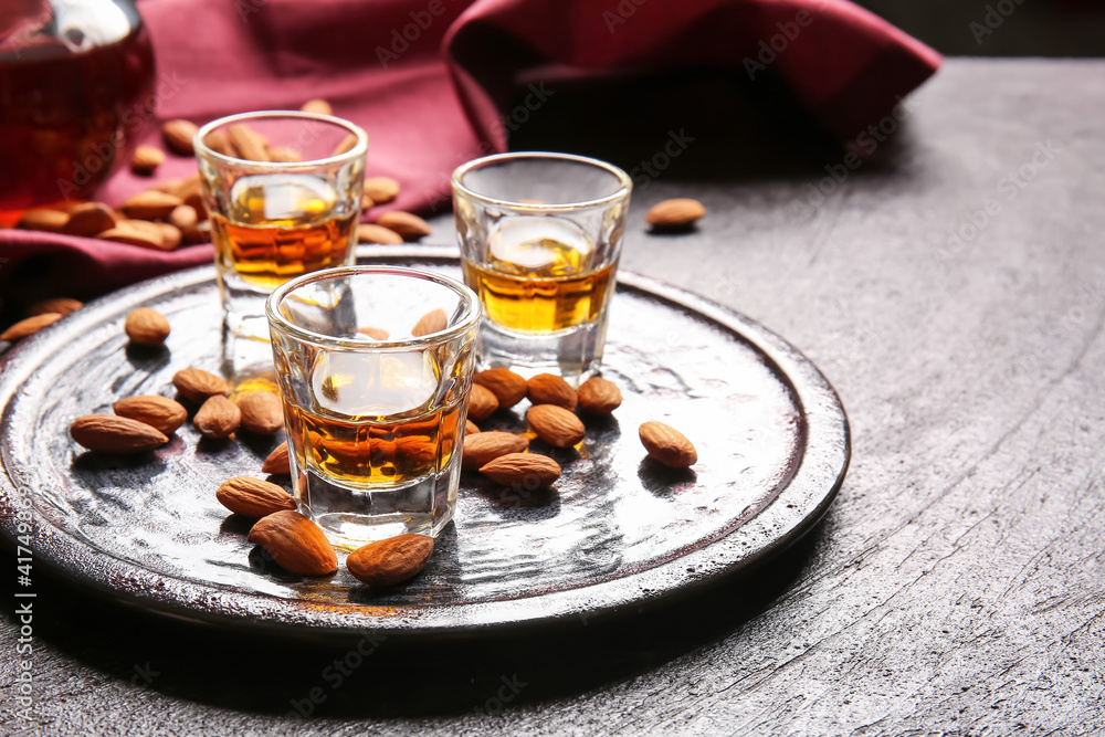 Tray with glasses of almond liquor and nuts on dark background