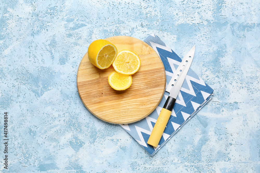 Wooden cutting board and lemon on color background