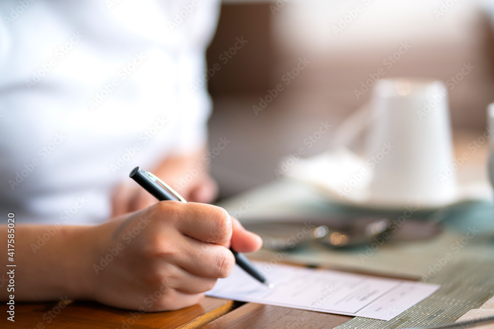 Closeup image of a hand writing on blank notebook or paper order filling form with coffee cup on tab