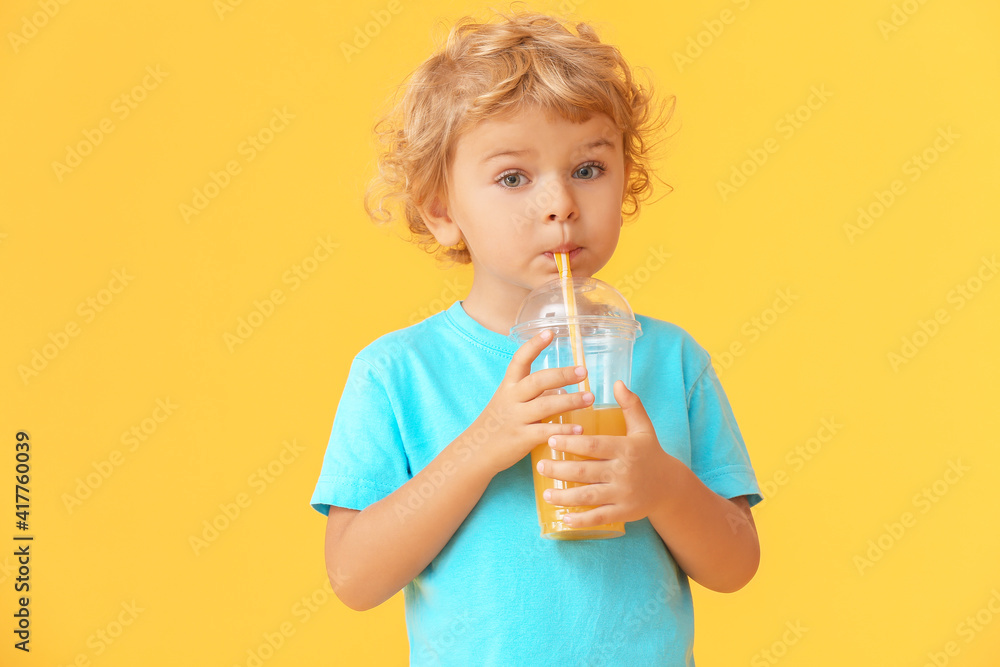 Cute little boy drinking orange juice on color background