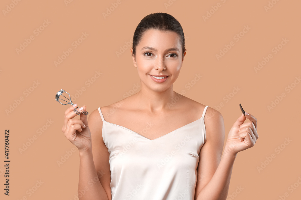 Beautiful young woman with fake eyelashes and curler on color background