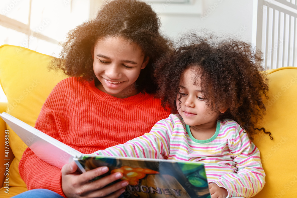 Cute African-American sisters reading book at home