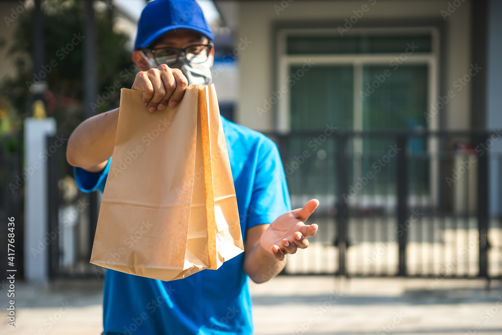 Asian delivery man wearing mask delivers pizza, customer in medical gloves signs on tablet. Delivery