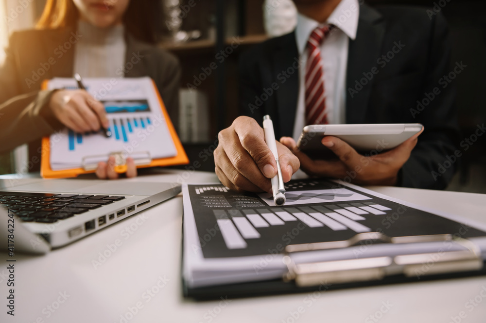 Business documents on office table with smart phone and laptop and two colleagues discussing data