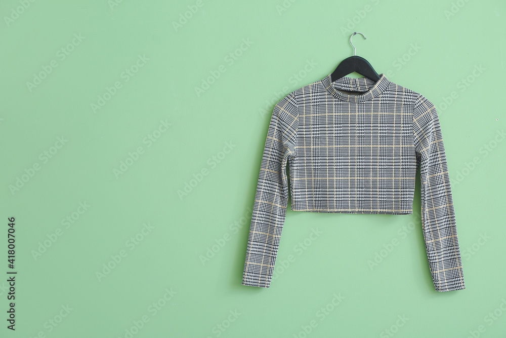 Hanger with stylish clothes on color background