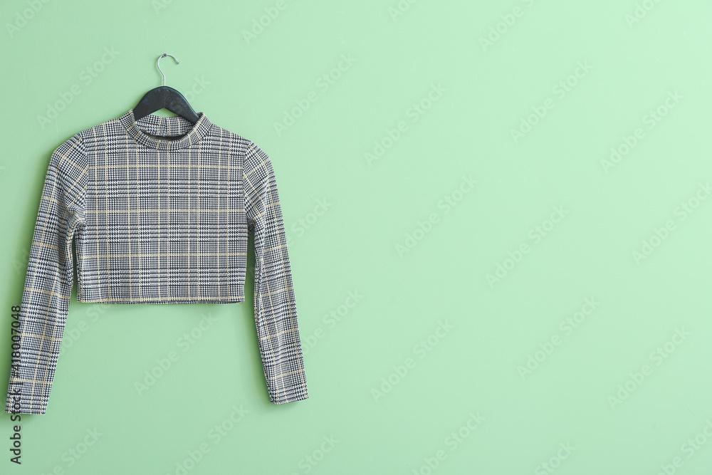 Hanger with stylish clothes on color background