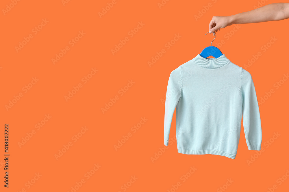 Woman holding hanger with sweater on color background