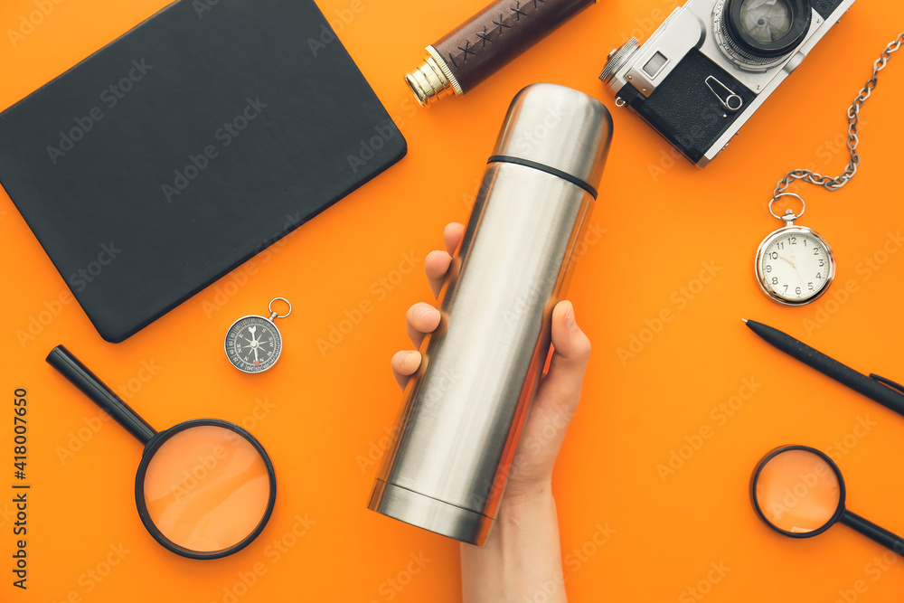 Female hand with modern thermos and items for travel on color background