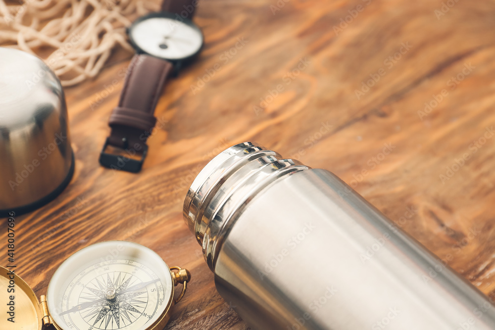 Modern thermos and items for travel on wooden background, closeup