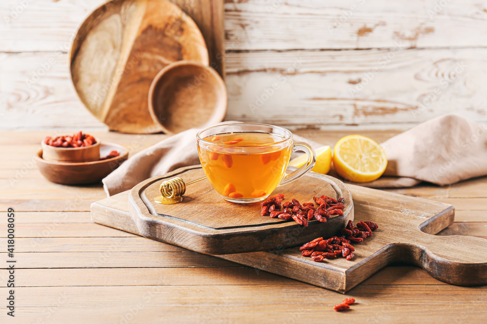 Glass cup of hot tea with goji berries on light wooden background