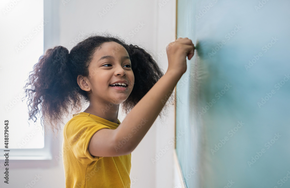 Closeup portrait of young happy African little girl write on chalk board. student writing on blackbo