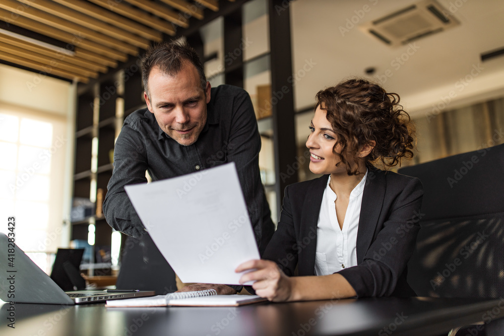 Two smiling manager looking at paper document, portrait.