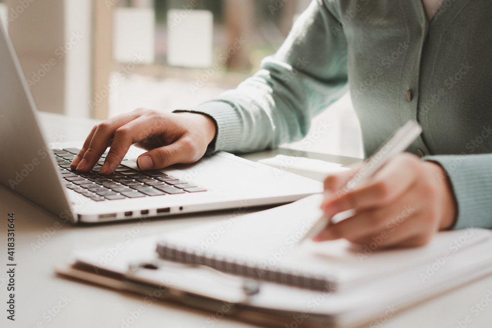 Business women work on computers and write on notepad with pen to calculate financial statements wit